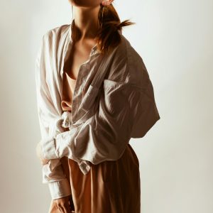 Trendy woman posing in oversized shirt and sunglasses, exuding modern fashion style.